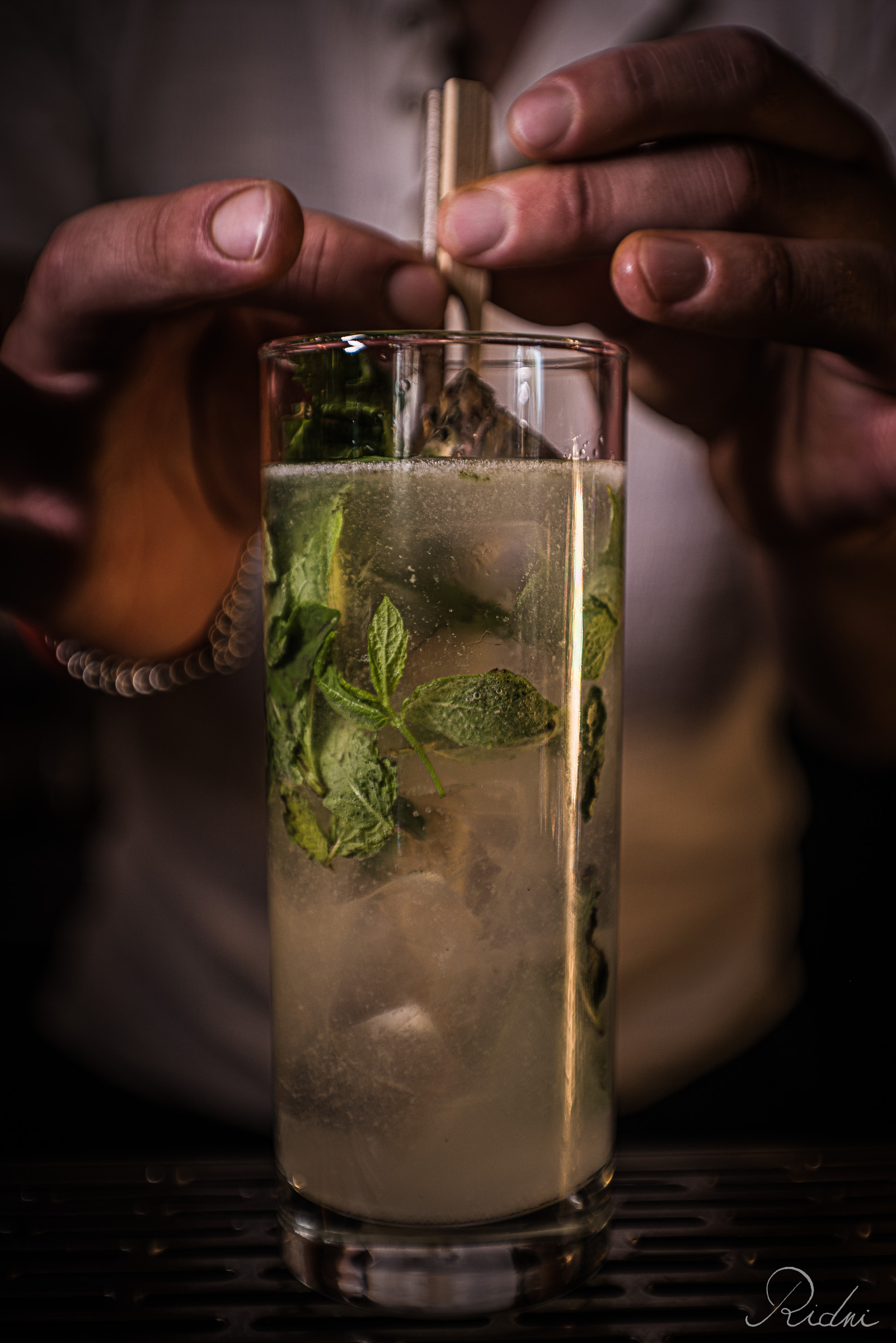 A bartender at bar Zona in lignano, friuli, prepares a fresh mint cocktail in a tall glass with precise movements.