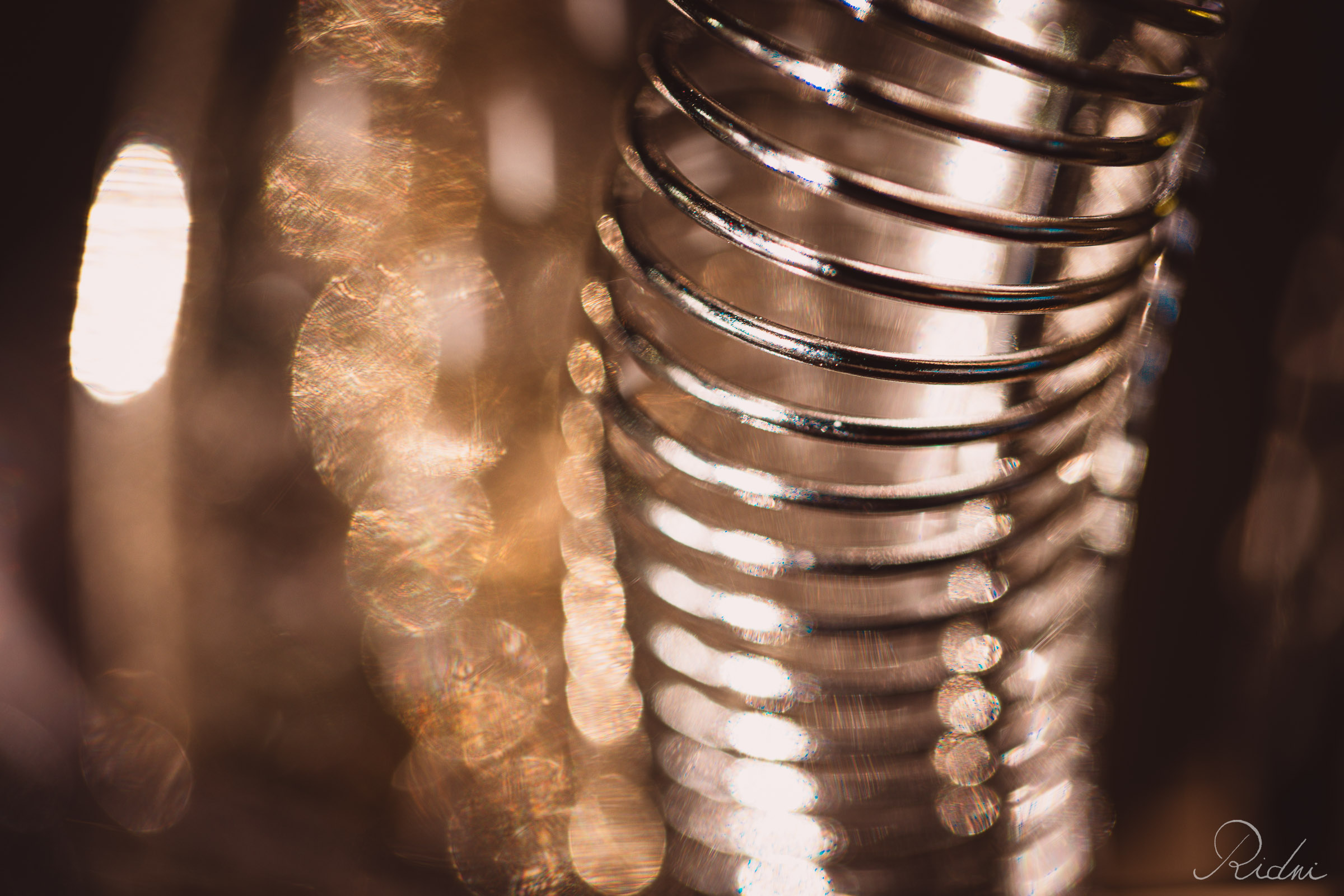 A macro view of a metallic bar tool spring at bar Zona in lignano, friuli, surrounded by warm, golden bokeh light.