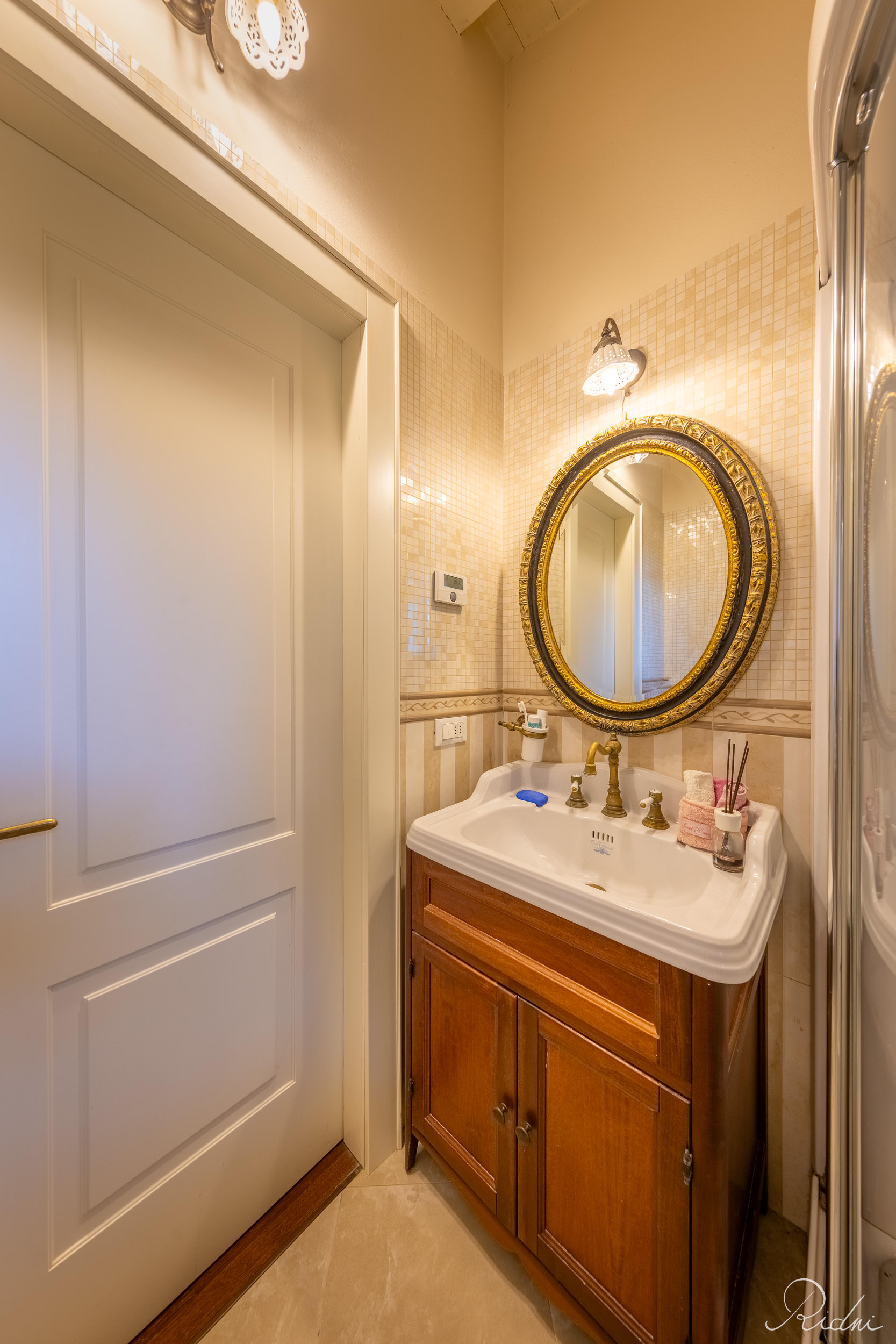 A wooden vanity with a white sink and ornate gold mirror in a warm bathroom, showcasing professional real estate photography.