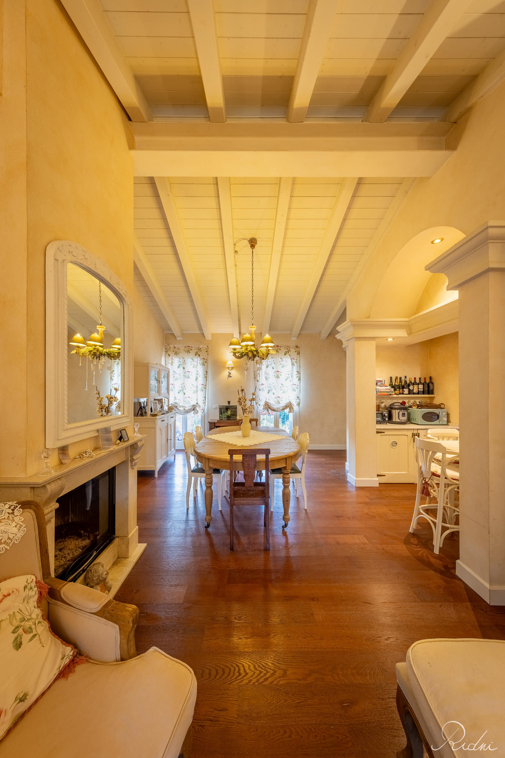 A warm dining room featuring a wooden table, white beamed ceiling, and fireplace, showcasing professional real estate photography.