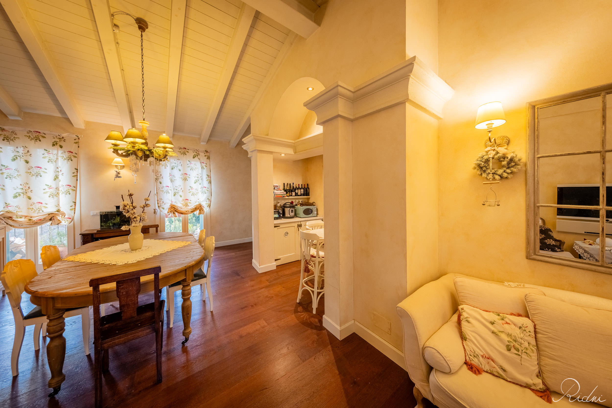 Rustic living area with a wooden table, beamed ceiling, and warm lighting, showcasing professional real estate photography in an Italian home.