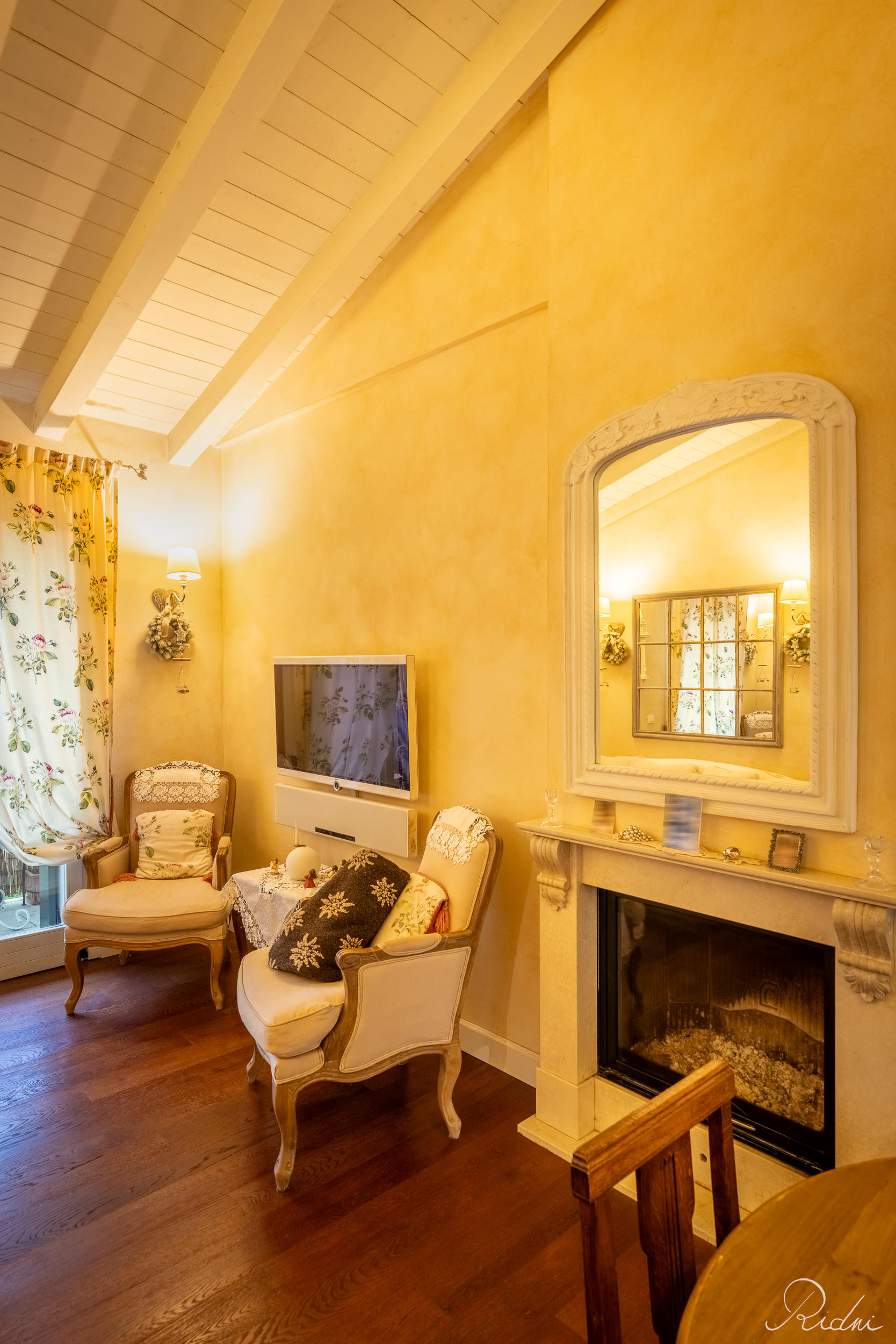A cozy living room captured through real estate photography, featuring yellow walls, a fireplace with a mirror, and elegant armchairs.